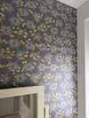 A romantic, maximalist wallpaper featuring a botanical, Japanese and Arts and Crafts-inspired pattern in metallics, blue, grey, pink and yellow, with a subtle shimmer, on a bedroom feature wall, by a window and dressing table mirror. Wild Lone's "Berry Galaxy" wallpaper in "Smoky Grey".