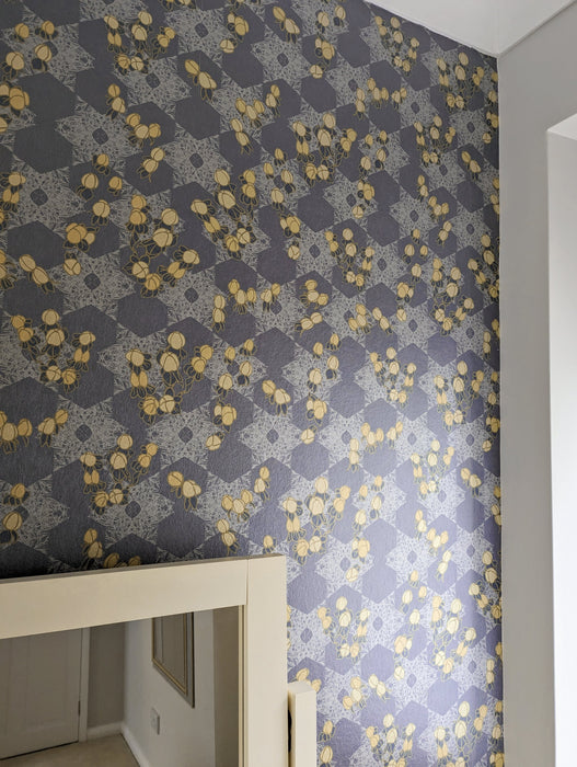 A romantic, maximalist wallpaper featuring a botanical, Japanese and Arts and Crafts-inspired pattern in metallics, blue, grey, pink and yellow, with a subtle shimmer, on a bedroom feature wall, by a window and dressing table mirror. Wild Lone's "Berry Galaxy" wallpaper in "Smoky Grey".