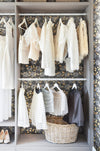 A feminine, romanic bedroom and wardrobe, with visible clothes hanging from wracks, and wallpaper behind it and on the adjoining wall. Wild Lone's "Berry Galaxy" wallpaper in "Smoky Grey", a whimsical, Arts and Crafts and Japanese-inspired wallpaper featuring blues, peaches and gold in a botanical design.