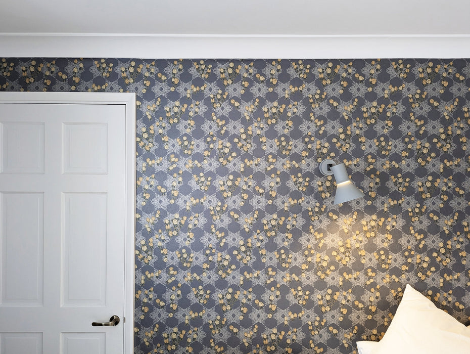 A romantic, maximalist wallpaper, with metallics, blue, grey, pink and yellow in a botanical, Japanese and Arts and Crafts-inspired pattern, with a subtle pearlescence, on a bedroom feature wall. Wild Lone's "Berry Galaxy" wallpaper in "Smoky Grey".