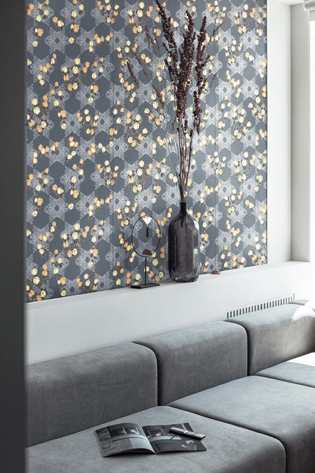 A luxurious, maximalist wallpaper featuring a botanical, Japanese and Arts and Crafts-style pattern in metallics, blue, grey, pink and yellow, with a subtle shimmer, in a modern living room with a grey sofa. Wild Lone's "Berry Galaxy" wallpaper in "Smoky Grey".