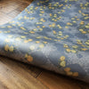 Wild Lone's "Berry Galaxy" wallpaper in "Smoky Grey", in a roll on floorboards. A romantic, Japanese and Arts and Crafts-inspired design featuring blues, peaches and gold, with a subtle pearlescence.