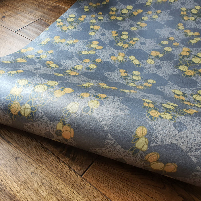 Wild Lone's "Berry Galaxy" wallpaper in "Smoky Grey", in a roll on floorboards. A romantic, Japanese and Arts and Crafts-inspired design featuring blues, peaches and gold, with a subtle pearlescence.