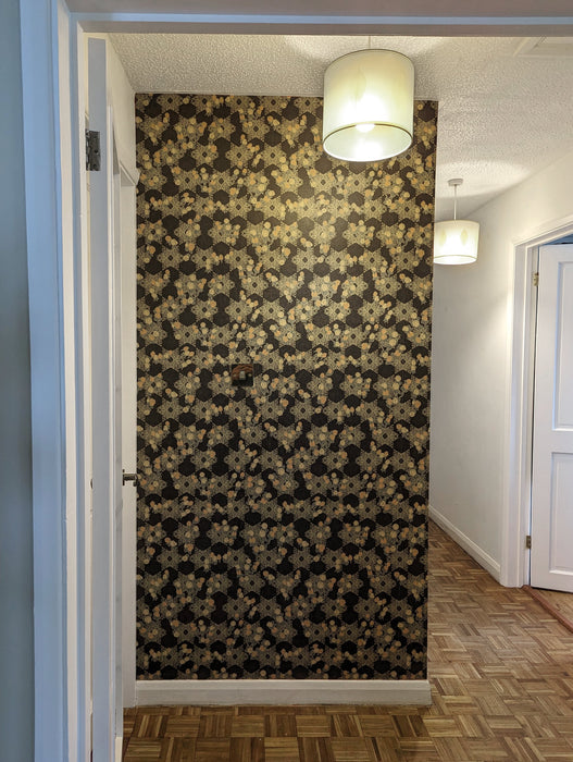  A dark, maximalist wallpaper with bright gold and peach decorative detail, in a botanical, Japanese and Arts and Crafts-inspired pattern. Wild Lone's "Berry Galaxy" wallpaper in "Warm Black", in a feature wall in a hallway.