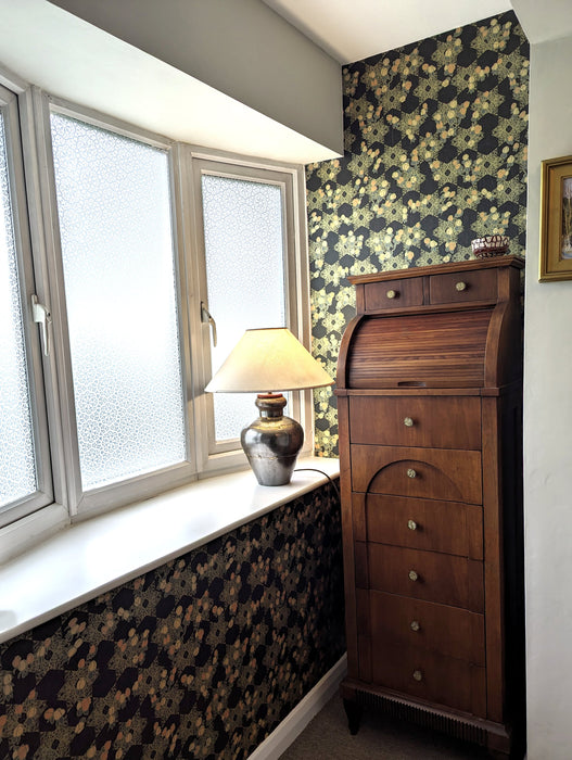 A maximalist, botanical and Japanese-style wallpaper, with a dark background and a metallic gold and peach pattern. Wild Lone's "Berry Galaxy" wallpaper in "Warm Black", in an entranceway.