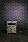 A dark, period interior with rustic furniture and floorboards, with a bold, moody and pearlescent wallpaper, featuring a botanical, Art Nouveau and Japanese-inspired pattern in purple, pink, greens and gold. Wild Lone's "Greenhouse" wallpaper in "Exotic Green".