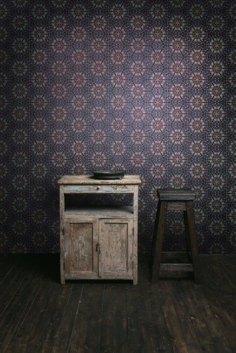A dark, period interior with rustic furniture and floorboards, with a bold, moody and pearlescent wallpaper, featuring a botanical, Art Nouveau and Japanese-inspired pattern in purple, pink, greens and gold. Wild Lone's "Greenhouse" wallpaper in "Exotic Green".