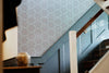A moody and intricate blue, pink and gold wallpaper, featuring an Art Nouveau and Japanese-inspired design, above blue wainscoting in a period stairwell. Wild Lone's "Greenhouse" wallpaper in "Ornamental Blue".