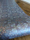 An exotic, bold and pearlescent wallpaper featuring blues, pinks and gold, in a botanical, Art Nouveau and Japanese-inspired design, in a roll on floorboards. Wild Lone's "Greenhouse" wallpaper in "Ornamental Blue".