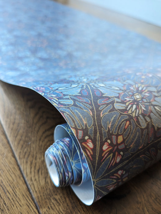 A closeup of a roll of Wild Lone's "Greenhouse" wallpaper in "Ornamental Blue", an intricate, Art Nouveau and Japanese-inspired design featuring a botanical pattern in blue, pink and gold.
