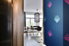 A luxurious, bold and statement wallpaper,  with a subtle pearlescence and a mood of dark romance, in a hallway in a light, eclectic apartment, featuring electric blue and magenta bee forms against a dark blue background. Wild Lone's "Night Flight" wallpaper in "Electric Blue".